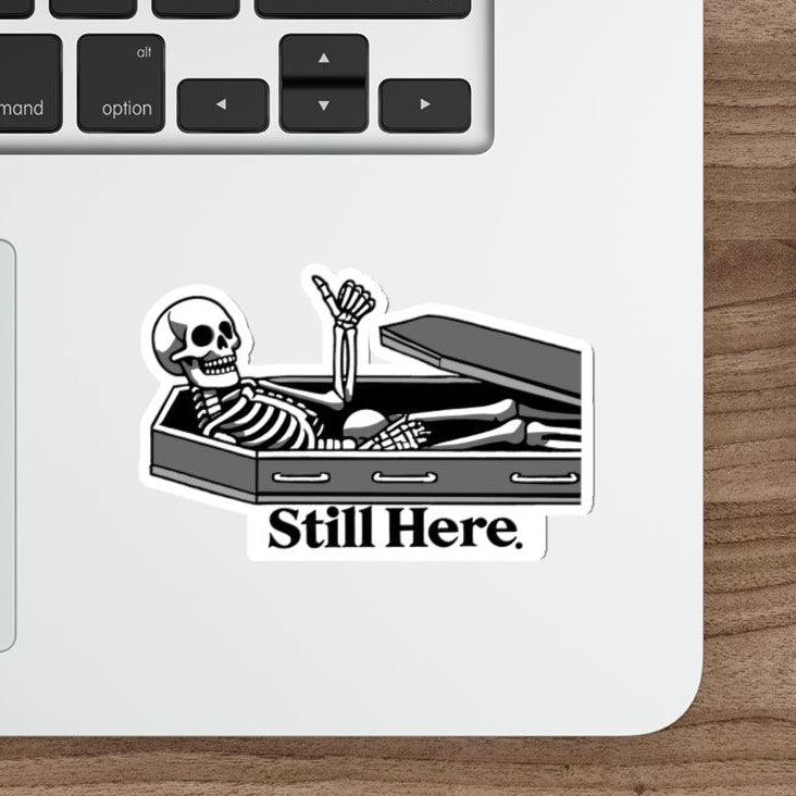 Still Here Skeleton Waterproof Sticker: A lounging skeleton with the phrase "Still Here," representing resilience with a humorous undertone, great for Halloween or everyday use.  KEOLIX 
