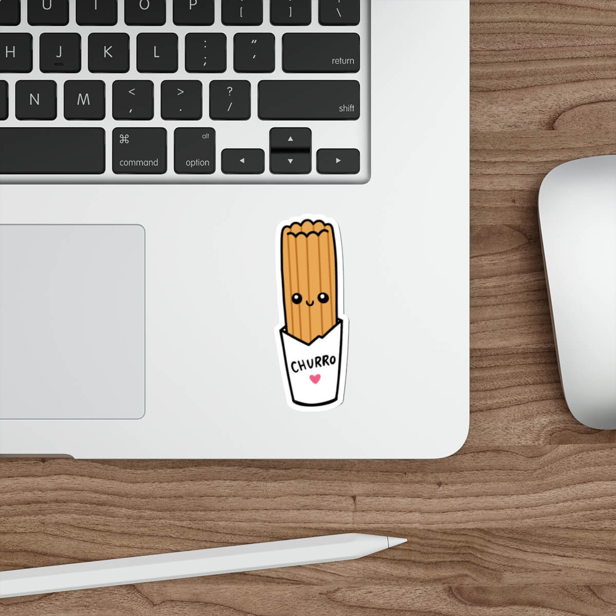A cute cartoon sticker of a churro in a paper cup with the word 'CHURRO' and a small pink heart, shown on the bottom corner of a silver laptop. The laptop sits on a wooden desk next to a white mouse and stylus.