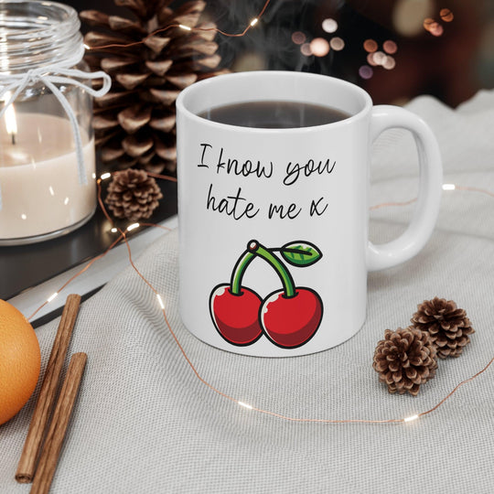White ceramic mug featuring a pair of cherries with the playful text 'I Know You Hate Me,' perfect for adding a bit of cheeky humor to your coffee routine.