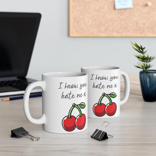 White ceramic mug featuring a pair of cherries with the playful text 'I Know You Hate Me,' perfect for adding a bit of cheeky humor to your coffee routine.