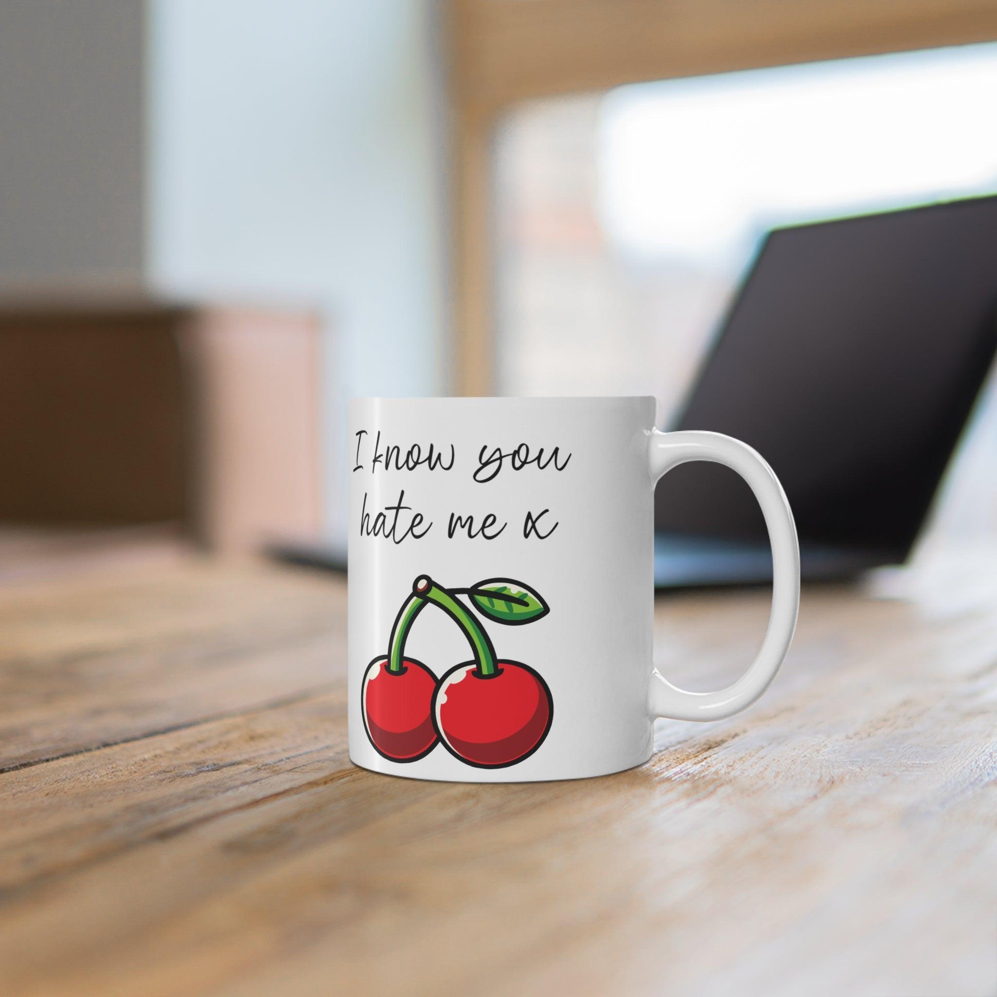 White ceramic mug featuring a pair of cherries with the playful text 'I Know You Hate Me,' perfect for adding a bit of cheeky humor to your coffee routine.