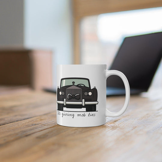 White ceramic mug featuring a black car design with the phrase 'It's Giving Mob Ties,' perfect for anyone with a love for mob-inspired humor.
