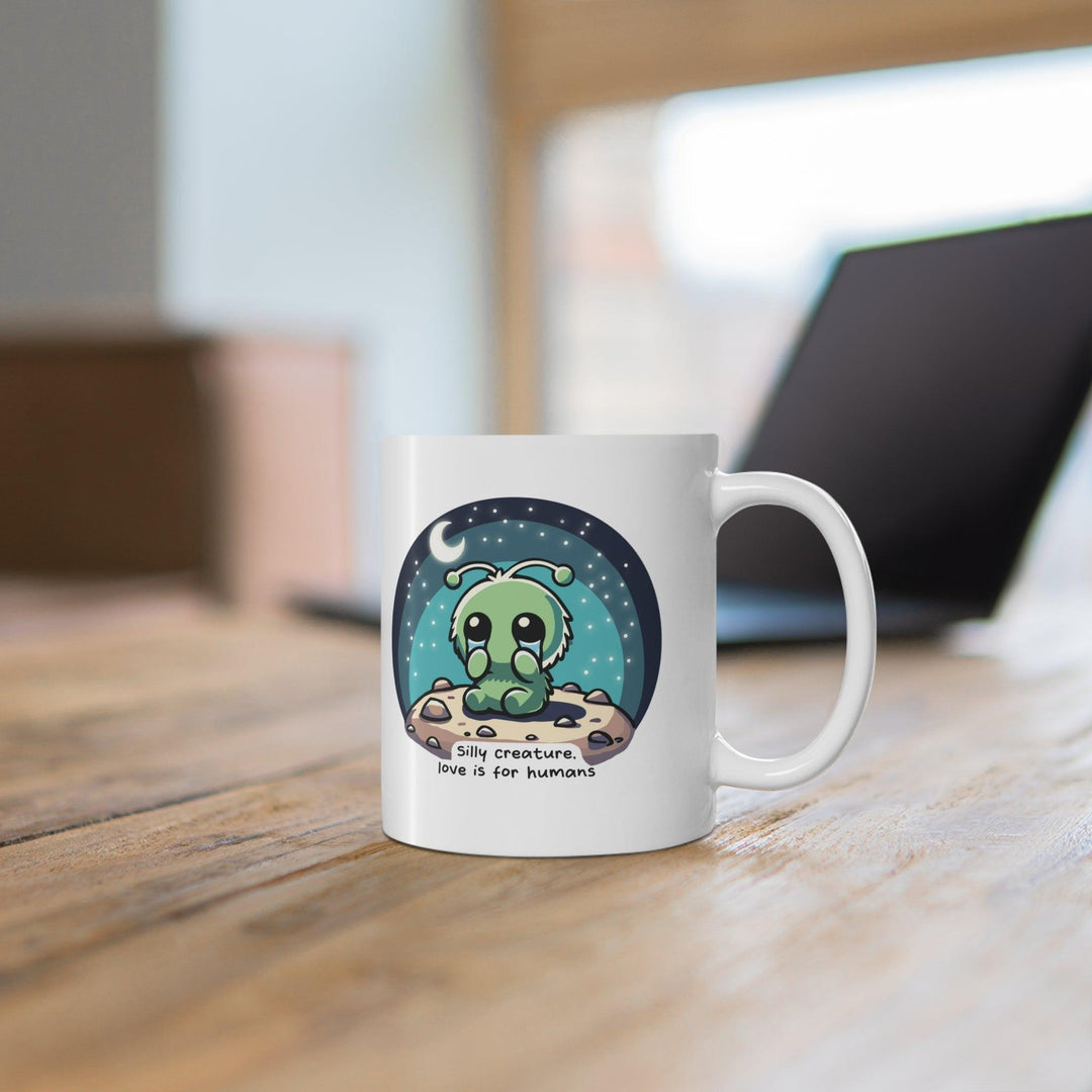 Fun white ceramic mug featuring cartoon creatures and the phrase 'Silly Creature, Love Is for Humans,' adding a whimsical and humorous touch."