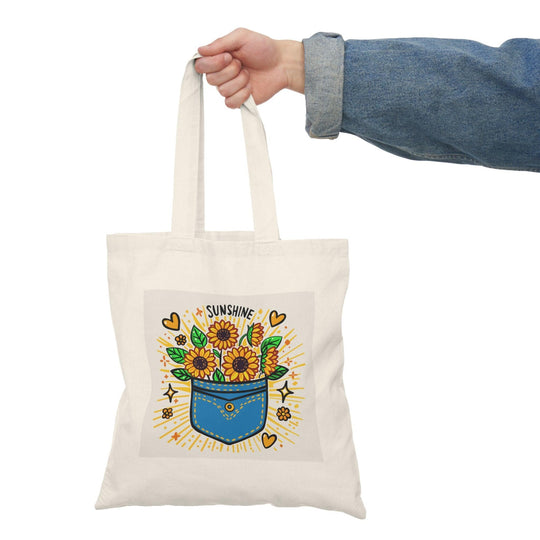 A natural tote bag adorned with a vibrant illustration of a flower pot filled with colorful flowers and the text 'Pocket Full of Sunshine.' The cheerful design radiates positivity and joy, making it a delightful accessory for spring and summer outings.
