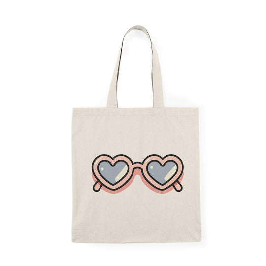 A natural canvas tote bag adorned with an artistic graphic of two overlapping heart shapes, symbolizing rose-tinted glasses. The text 'Life Through Rose Tinted Glasses' is playfully integrated into the design, reflecting a positive outlook and love for life.