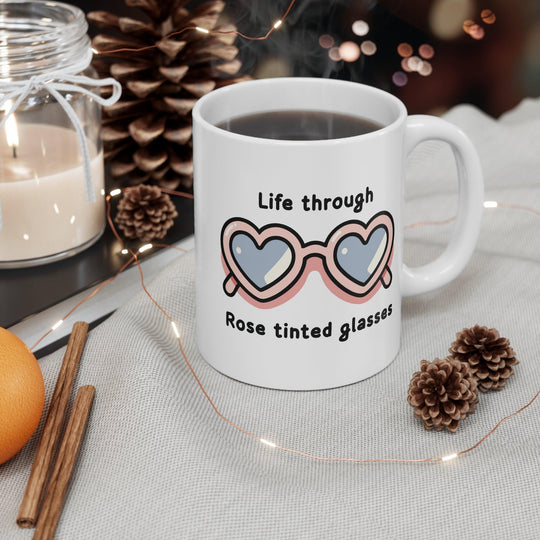 Charming white ceramic mug featuring heart-shaped sunglasses and the phrase 'Life Through Rose Tinted Glasses,' perfect for adding a positive outlook to your coffee time.