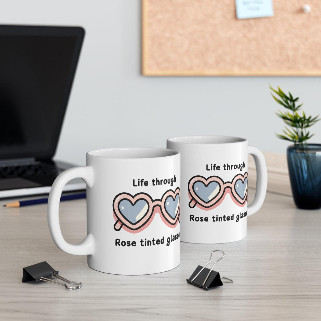 Charming white ceramic mug featuring heart-shaped sunglasses and the phrase 'Life Through Rose Tinted Glasses,' perfect for adding a positive outlook to your coffee time.