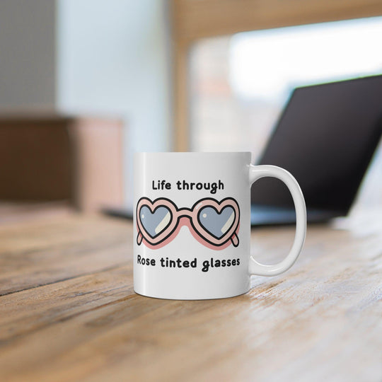 Charming white ceramic mug featuring heart-shaped sunglasses and the phrase 'Life Through Rose Tinted Glasses,' perfect for adding a positive outlook to your coffee time.