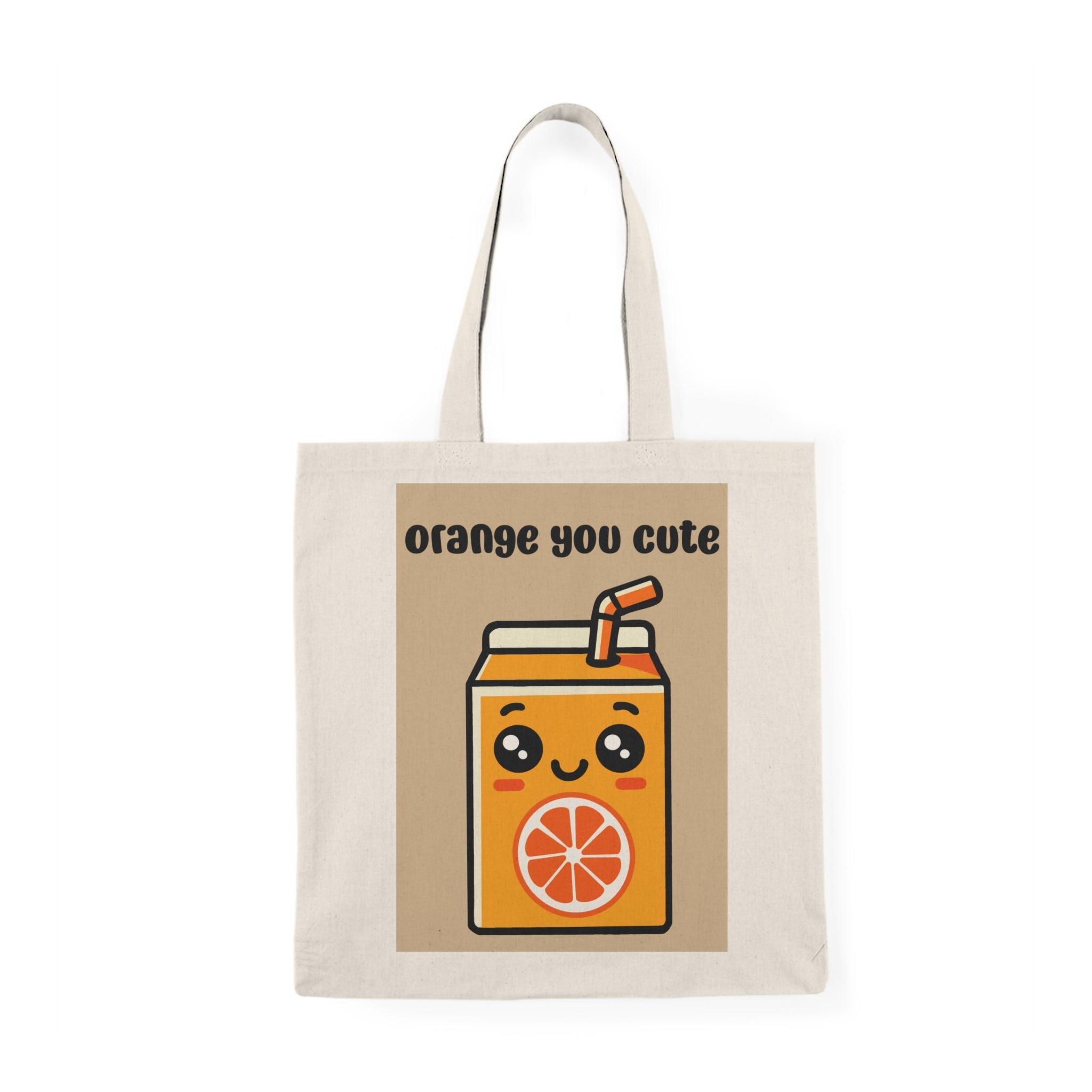 A cream-colored tote bag featuring an adorable graphic of a cartoon-style orange juice carton with a smiling face and the text 'Orange You Cute' in a playful font. This cheerful design adds a fruity flair, perfect for brightening up any casual outfit