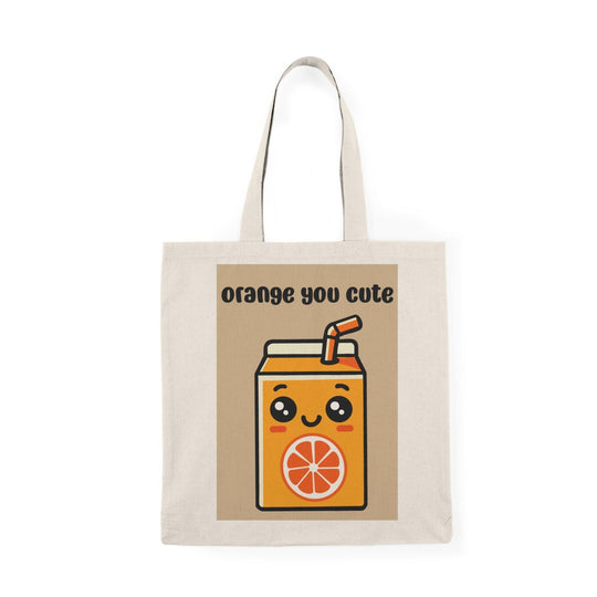 A cream-colored tote bag featuring an adorable graphic of a cartoon-style orange juice carton with a smiling face and the text 'Orange You Cute' in a playful font. This cheerful design adds a fruity flair, perfect for brightening up any casual outfit