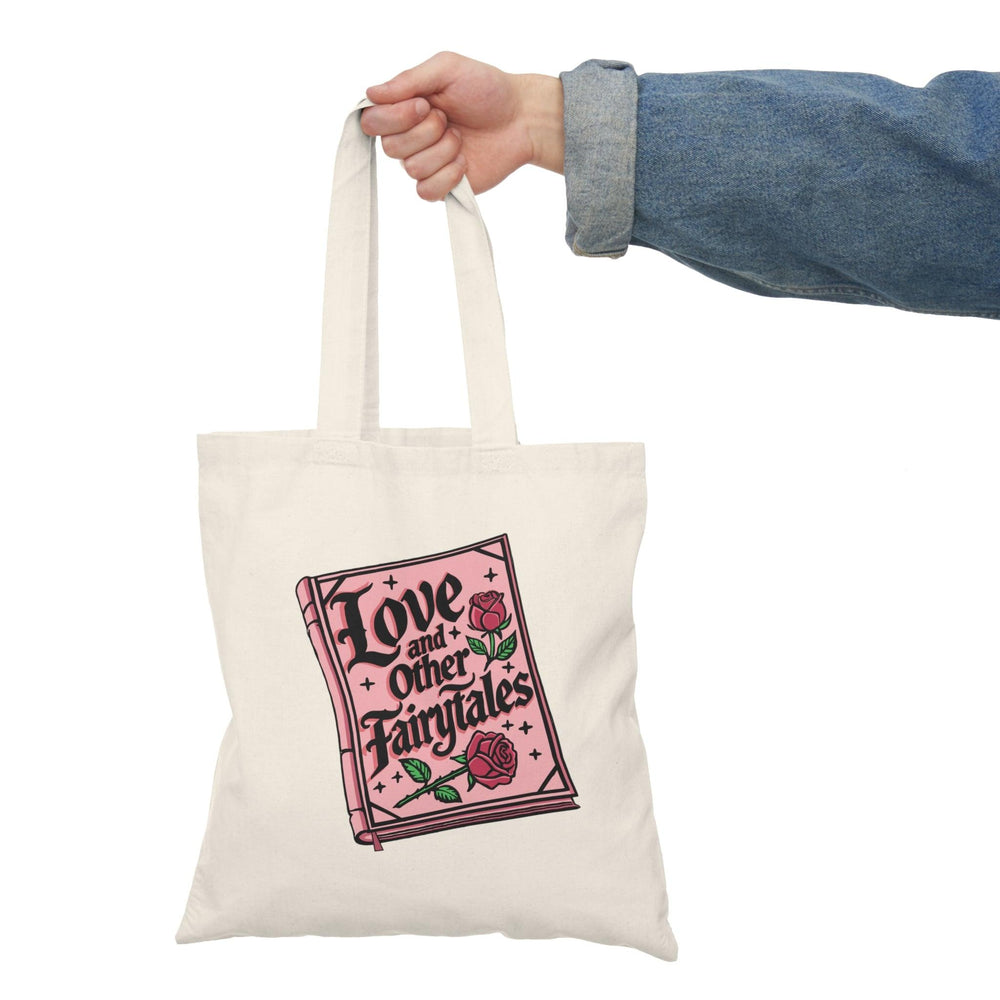 A natural canvas tote bag featuring a whimsical illustration with the text 'Love and Other Fairytales' surrounded by decorative elements. The enchanting design evokes a sense of magic and romance, making it an ideal accessory for dreamers and romantics