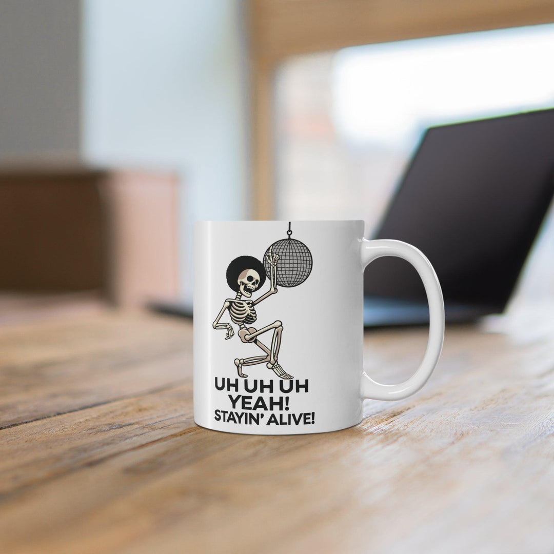 White ceramic mug with a disco-themed illustration and the text 'Stayin' Alive,' a fun, nostalgic nod to classic dance tunes