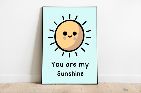 Brighten up your space with our charming "You are my Sunshine" framed print! This delightful piece features a cartoon sun with adorable rosy cheeks against a serene light blue background. Its lively black rays and joyful text add a cheerful touch, perfect for any room. Displayed leaning effortlessly against a white wall on a cozy wooden floor, it's sure to bring smiles and warmth to your home decor!