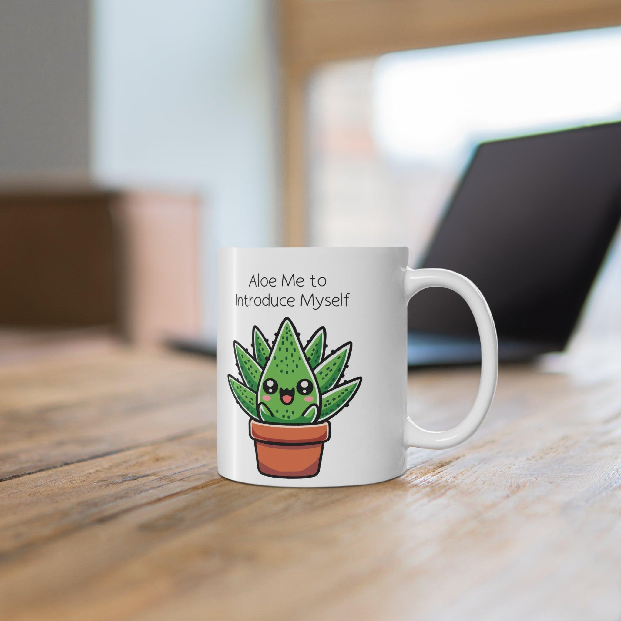 White ceramic mug showcasing a cute aloe plant in a pot with the pun 'Aloe Me to Introduce Myself,' surrounded by a warm, cozy ambiance