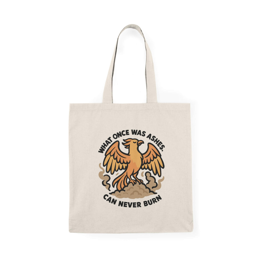 Tote bag with a fierce orange phoenix rising from smoke with bold black text that reads: "What once was ashes can never burn."