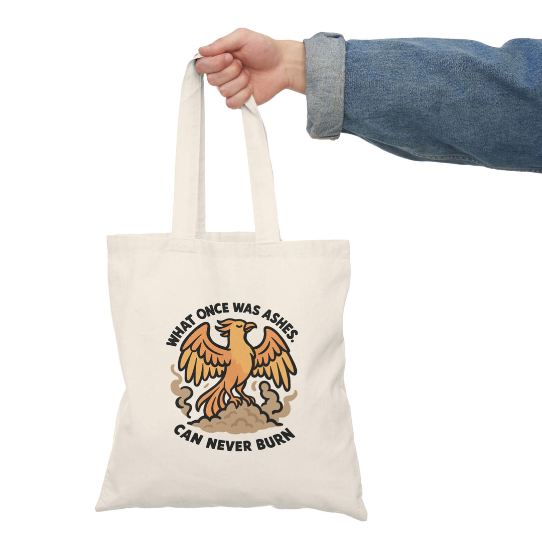  Tote bag with a fierce orange phoenix rising from smoke with bold black text that reads: "What once was ashes can never burn."