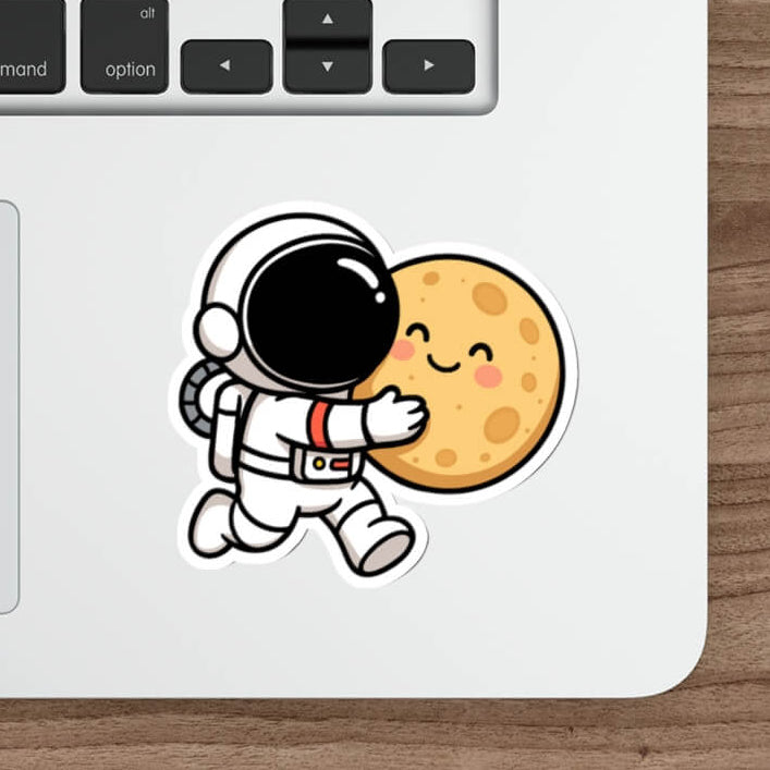 Cute vinyl sticker of a cartoon astronaut hugging a smiling moon, placed on a skateboard deck.