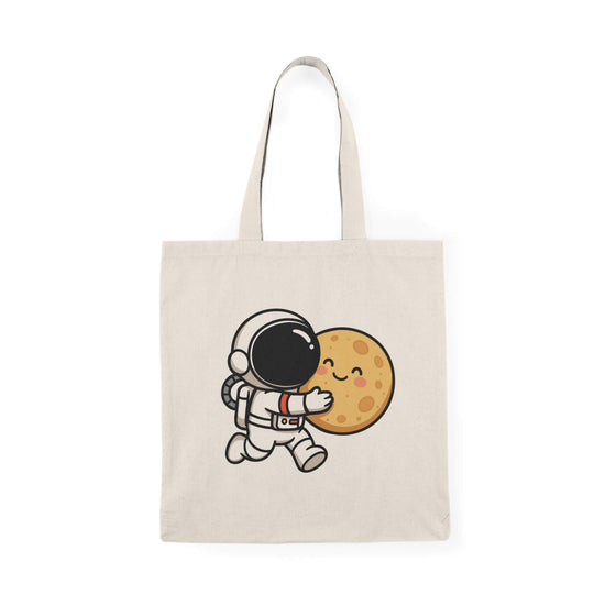 Natural cotton tote bag with a cute cartoon astronaut hugging a smiling moon, held by a hand in a denim jacket.