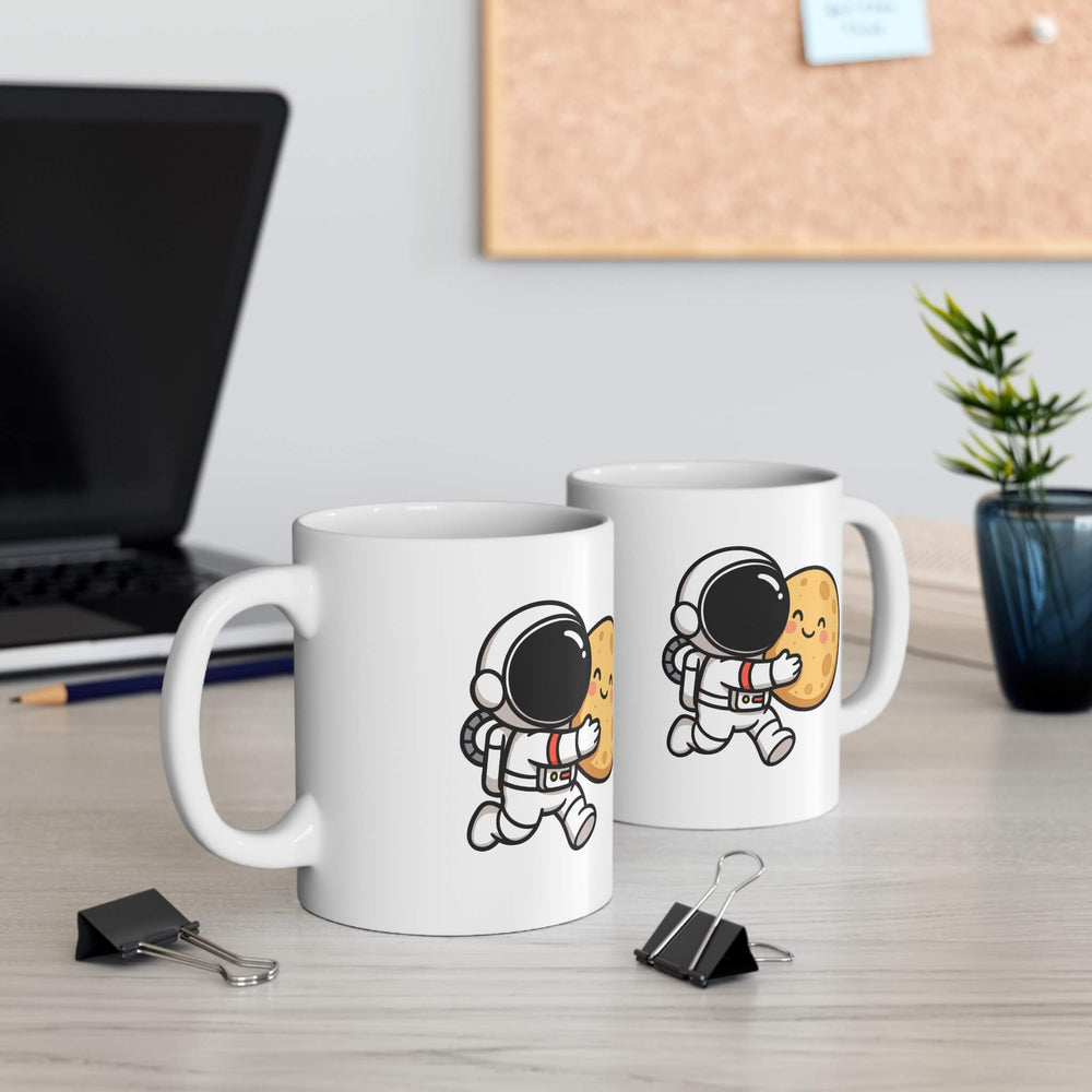 White ceramic mug with a cute cartoon astronaut hugging a smiling moon. Styled with pinecones and cozy winter decor.