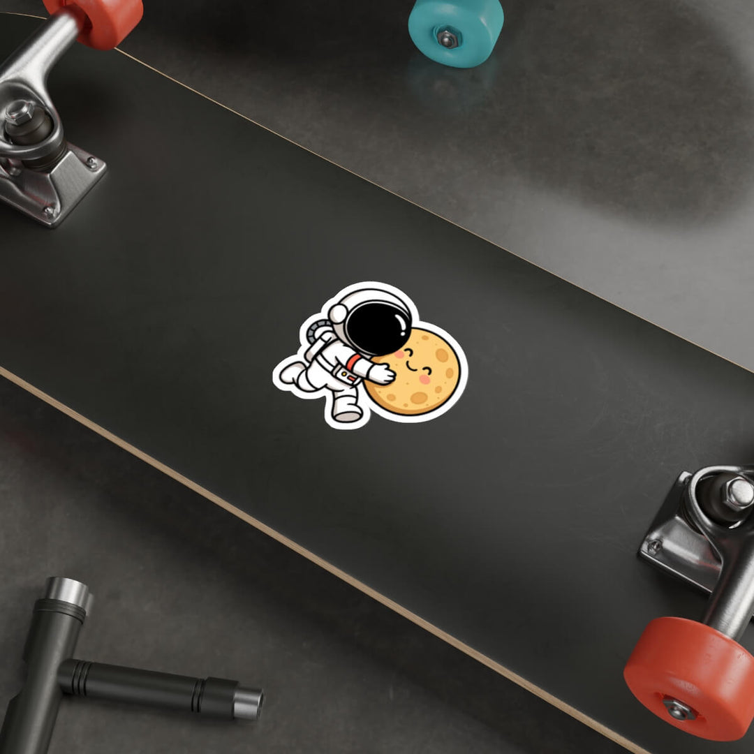 Cute vinyl sticker of a cartoon astronaut hugging a smiling moon, placed on a skateboard deck.