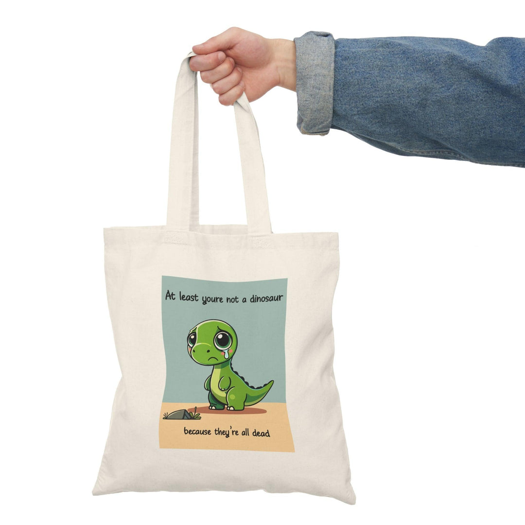Tote bag featuring a humorous illustration with the phrase 'At Least You're Not a Dinosaur.' The playful design incorporates whimsical graphics and bright colors, adding a lighthearted touch to your everyday carry while making a fun statement.