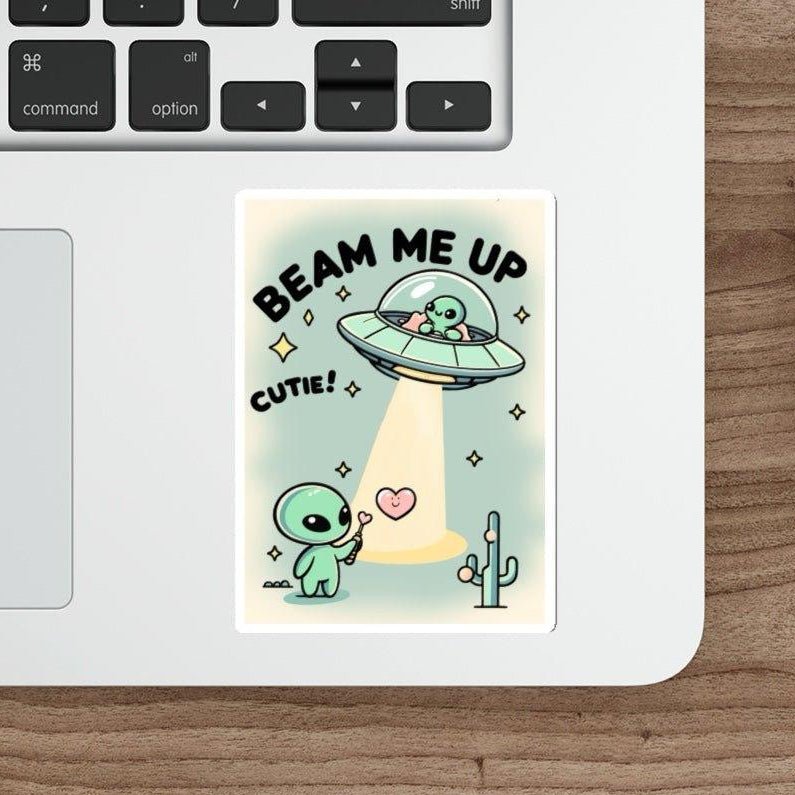 A sticker from  KEOLIX "Beam Me Up, Cutie" collection playfully adorns a laptop beside a mouse, featuring a cartoon alien being whisked away by a UFO. The text proudly declares "BEAM ME UP CUTIE!" amidst twinkling hearts and stars, with a charming cactus adding to this whimsical cosmic scene.