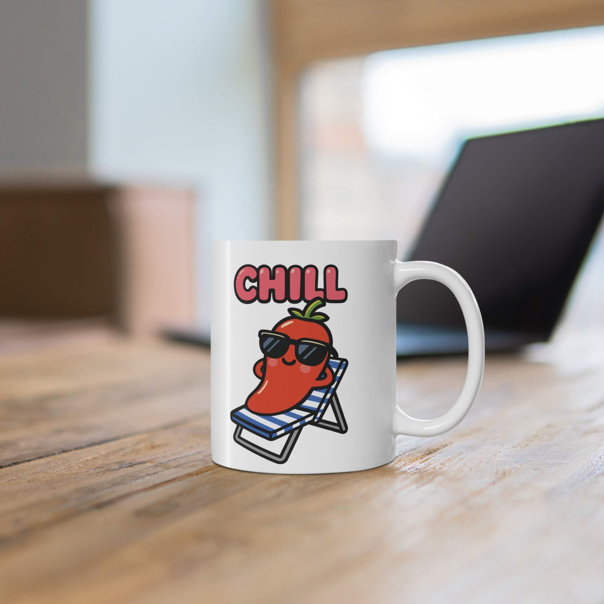 Funny cartoon red pepper wearing sunglasses, lounging on a striped deck chair with the word “CHILL” above, printed on a white ceramic mug placed on a wooden table.

