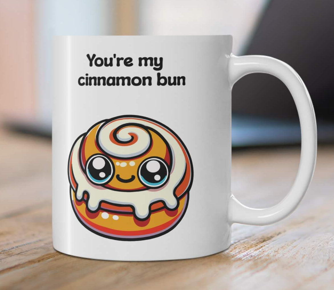 A charming ceramic mug with the phrase "You're my cinnamon bun" and a kawaii-style cinnamon bun illustration, set in a cozy holiday setting with cinnamon sticks and pine cones, enhancing a warm, festive atmosphere.

