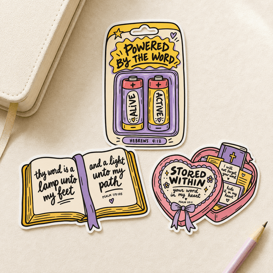 Three die-cut stickers displayed on a light beige textured surface with a cream notebook and a pink pencil. The stickers feature Bible verse quotes and religious-themed illustrations: one battery pack sticker reading &
