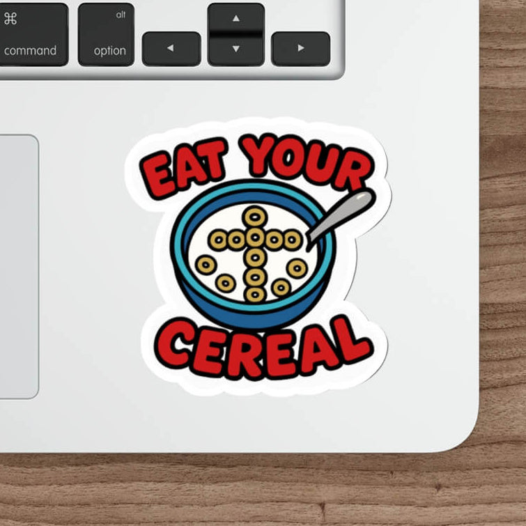 Christian cereal sticker featuring a bowl of Cheerios shaped into a cross with the text “Eat Your Cereal” in bold red font, placed on a laptop.