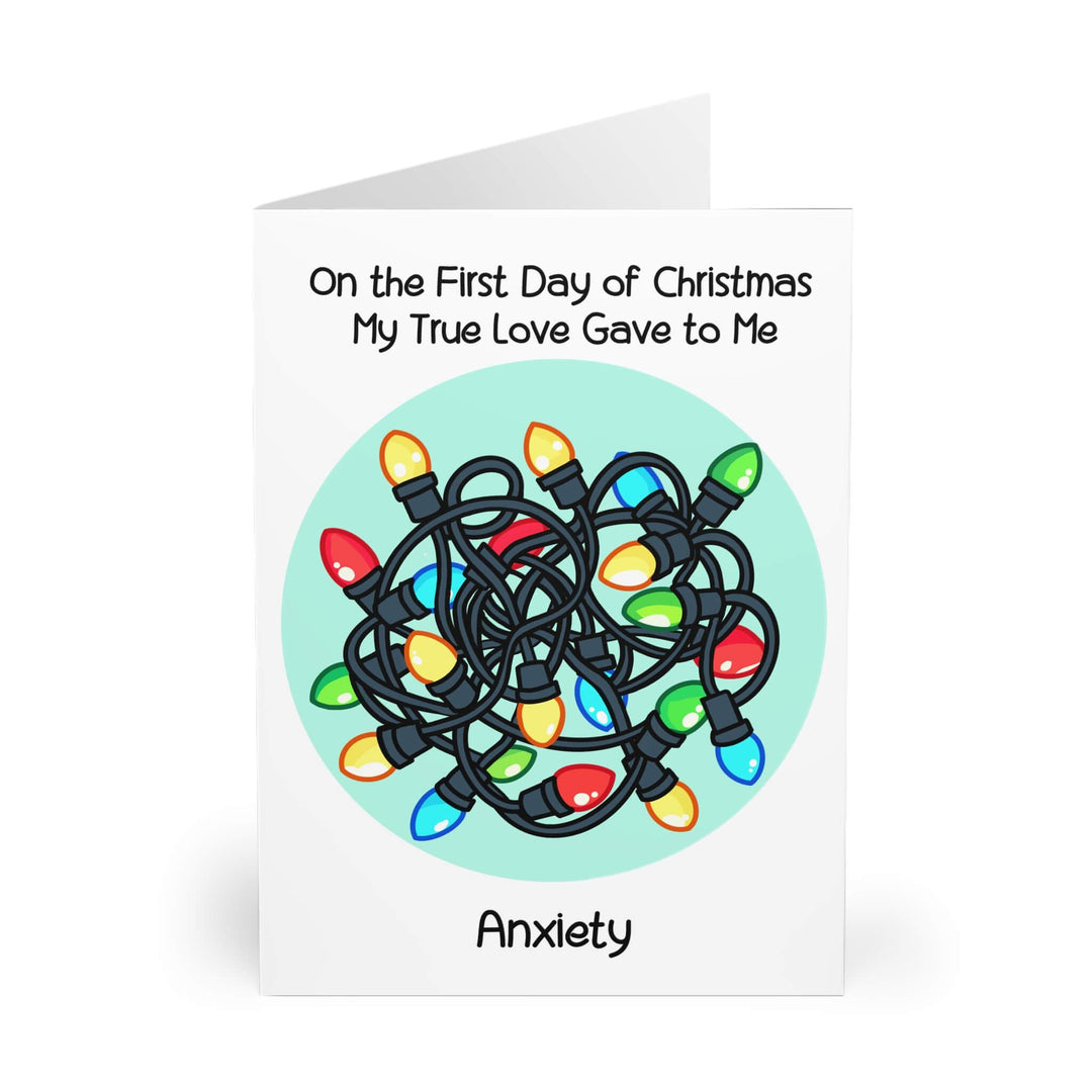 Humorous Christmas card featuring tangled Christmas lights with the phrase 'On the First Day of Christmas My True Love Gave to Me... Anxiety,' highlighting holiday stress and relatability. Perfect for sending a light-hearted message to loved ones during the Christmas season. Available in A5, 5x7, and A6 sizes.