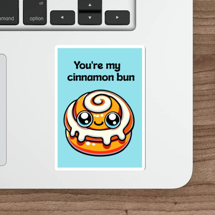 A whimsical sticker depicting a kawaii-style cinnamon bun with a caption "You're my cinnamon bun" placed on a laptop, adding a personal and affectionate touch to everyday technology.