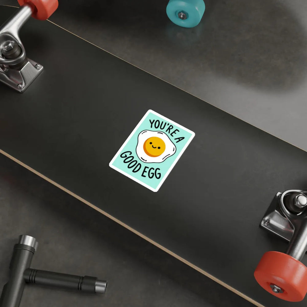 A fun and playful waterproof sticker featuring a fried egg with a smiling face and the phrase "You're a Good Egg" on a pastel teal background.