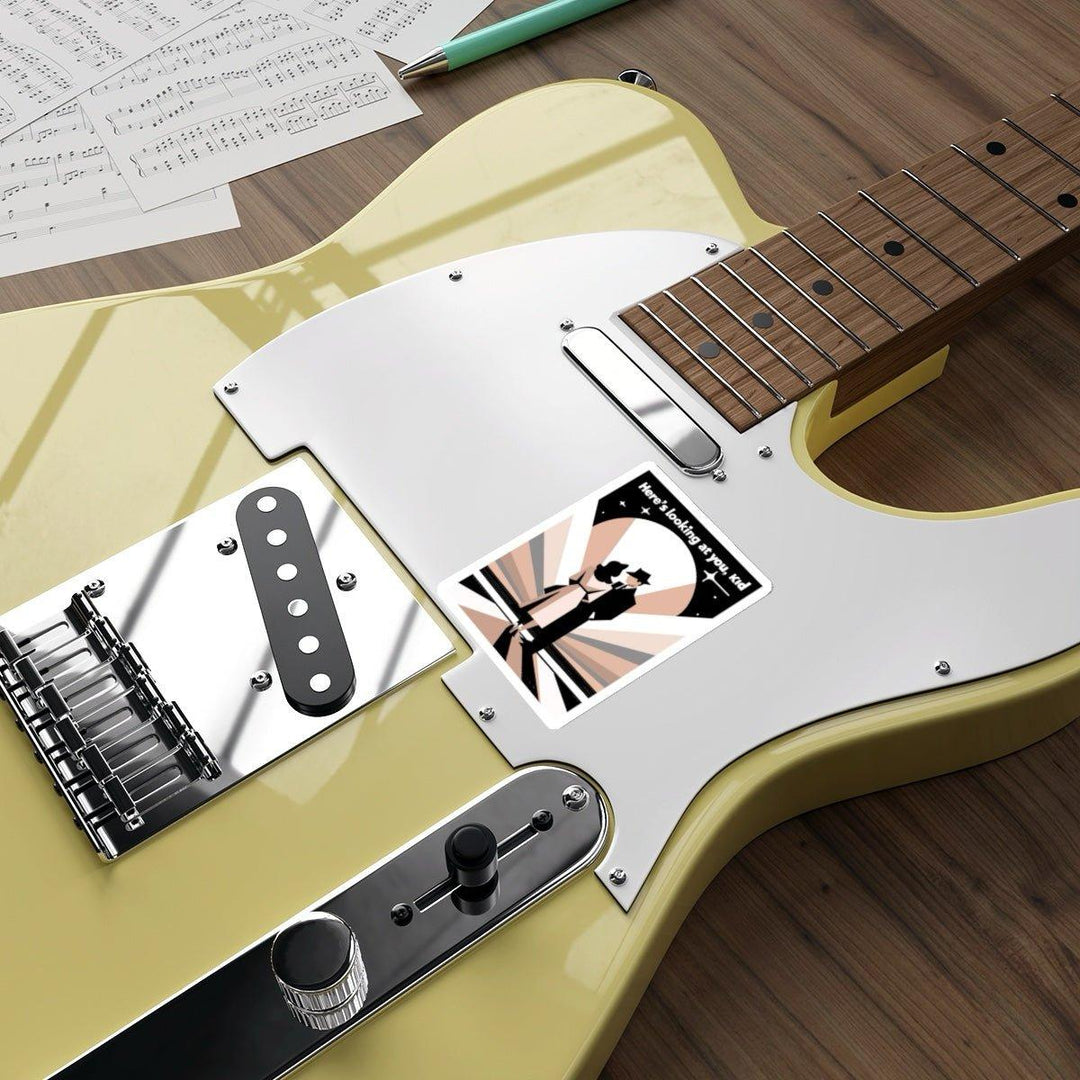 A yellow electric guitar with a white pickguard rests on a wooden surface. The "Here&