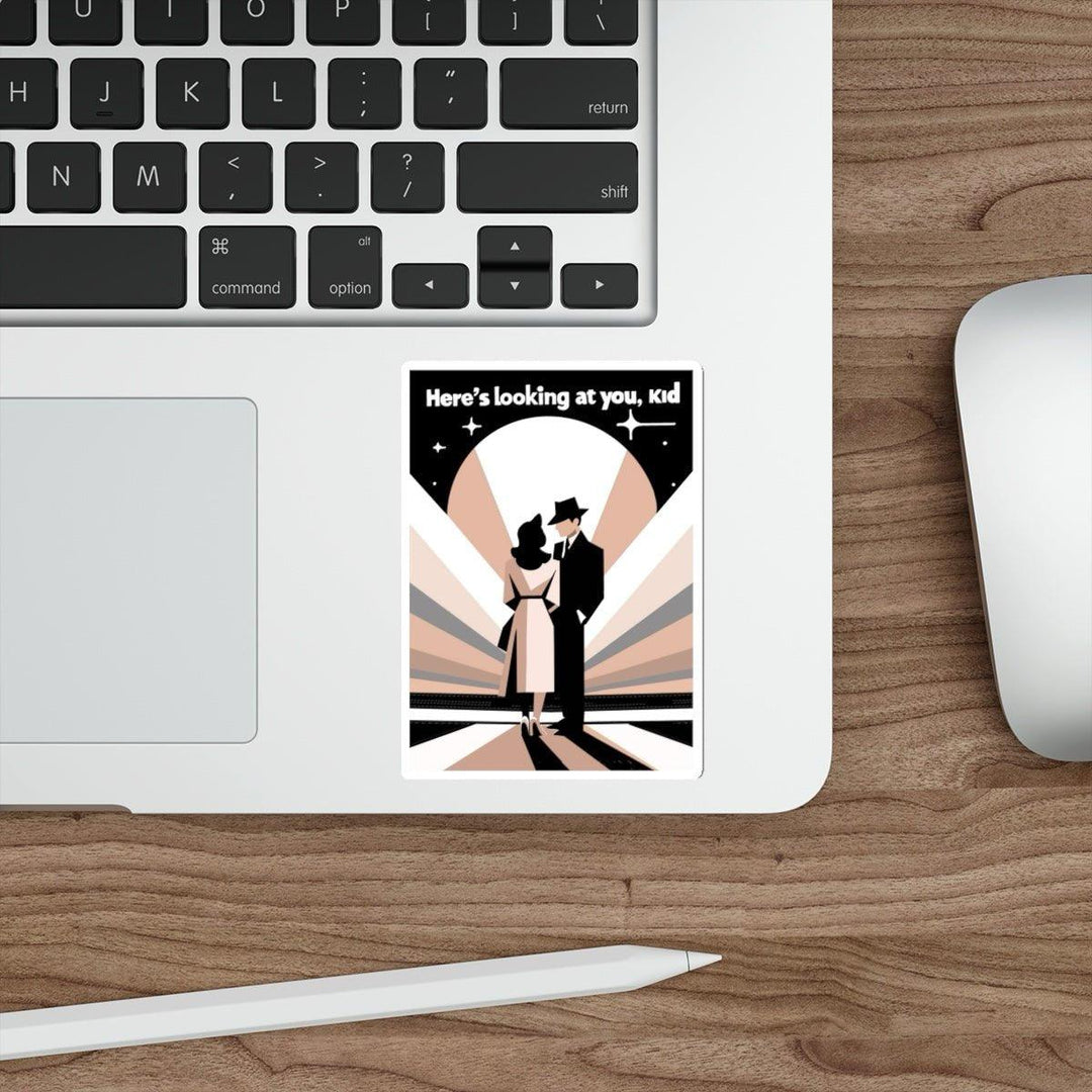 A laptop rests on a wooden desk. Beside it, a white computer mouse is positioned to the right. Near the touchpad, a "Here's Looking at You, Kid" waterproof sticker from Baby Keo captures vintage glamour with a silhouette of a couple in timeless attire and the iconic phrase.