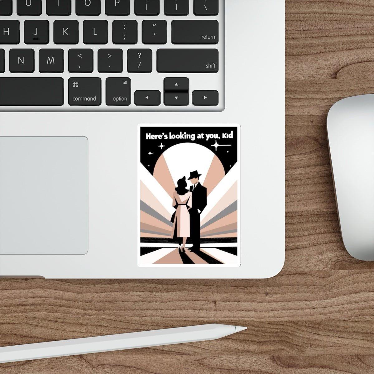 A laptop rests on a wooden desk. Beside it, a white computer mouse is positioned to the right. Near the touchpad, a "Here's Looking at You, Kid" waterproof sticker from Baby Keo captures vintage glamour with a silhouette of a couple in timeless attire and the iconic phrase.
