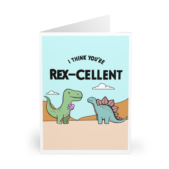 The "I Think Your Rex-cellent" Card by Baby Keo showcases charming cartoon dinosaurs, with a T-Rex holding a heart and facing a Stegosaurus. Set in a desert landscape with the text "I think you're rex-cellent," this Dinosaur Card adds charm to any occasion.