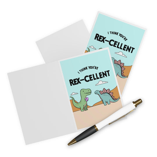 Two whimsical "I Think You're Rex-cellent" cards by Baby Keo feature a sandy background with a charming dinosaur holding a flower. Accompanied by a white pen adorned with black and gold accents, these personalized cards are ideal for making someone feel truly special.