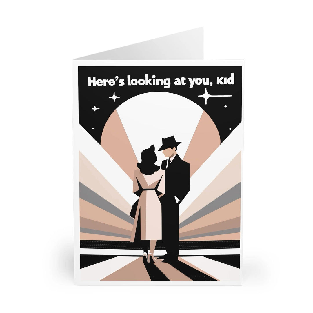 Casablanca-inspired greeting card featuring a minimalist design of a couple in retro attire, silhouetted against a backdrop of rays. The phrase 'Here's looking at you, kid' is printed at the top, capturing the iconic scene from the classic film.