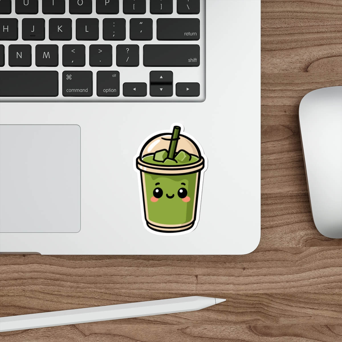 Glossy vinyl sticker of a smiling matcha drink in a dome-lid cup with blush cheeks and a straw, styled on a laptop next to a keyboard and pen.

