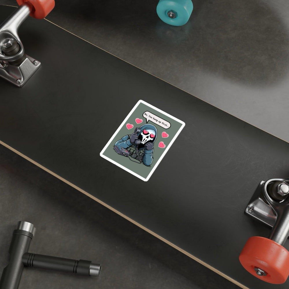 A skateboard is lying on the ground with a humorous design. In the center, there's a "No, You Hang Up First..." waterproof sticker by Baby Keo featuring a cute skull character surrounded by pink hearts and holding a phone. The text reads, "I hope you get that." Its orange and blue wheels add a pop of color to this personalized ride.