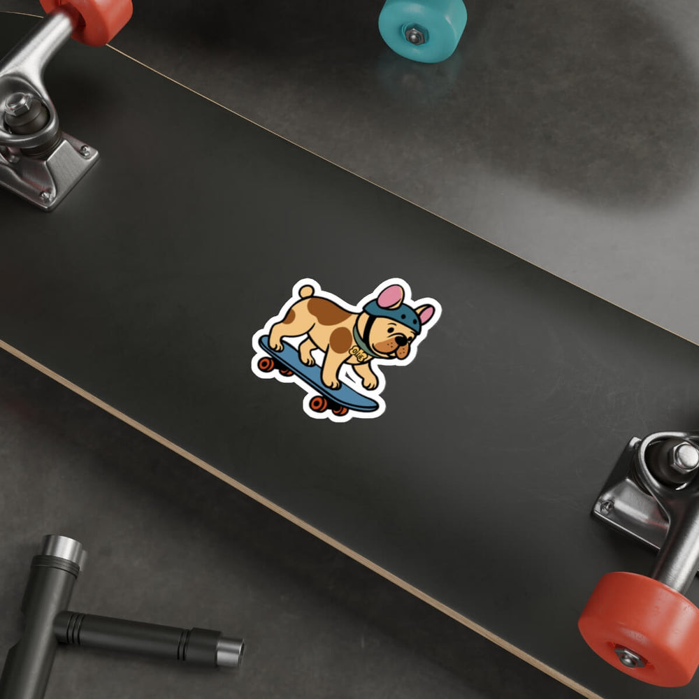Vinyl sticker of a cartoon French bulldog wearing a helmet and riding a skateboard, placed on a silver laptop beside a white pen and keyboard.