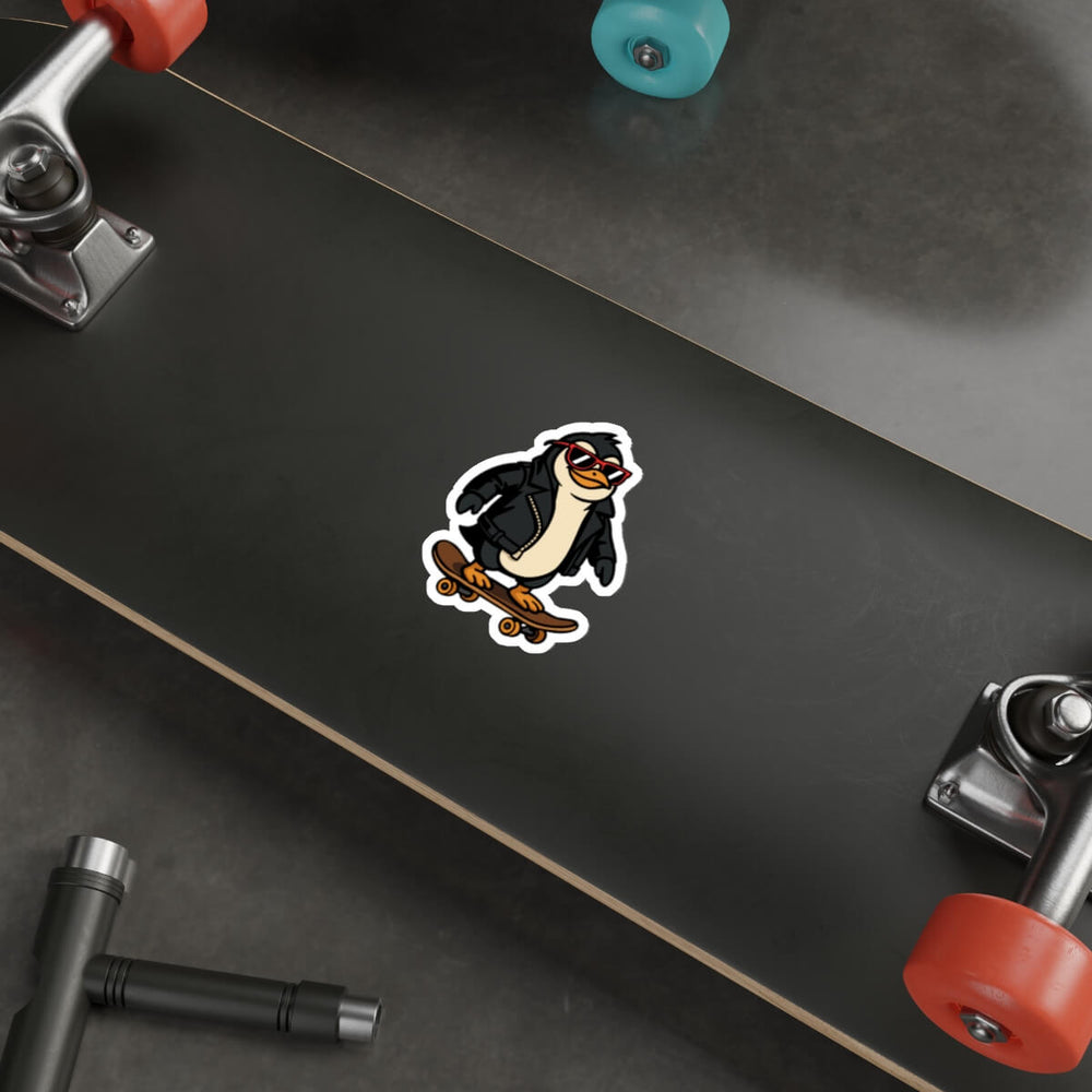 Sticker of a cartoon penguin in a black leather jacket and red sunglasses riding a skateboard, placed on a laptop next to a pencil.
