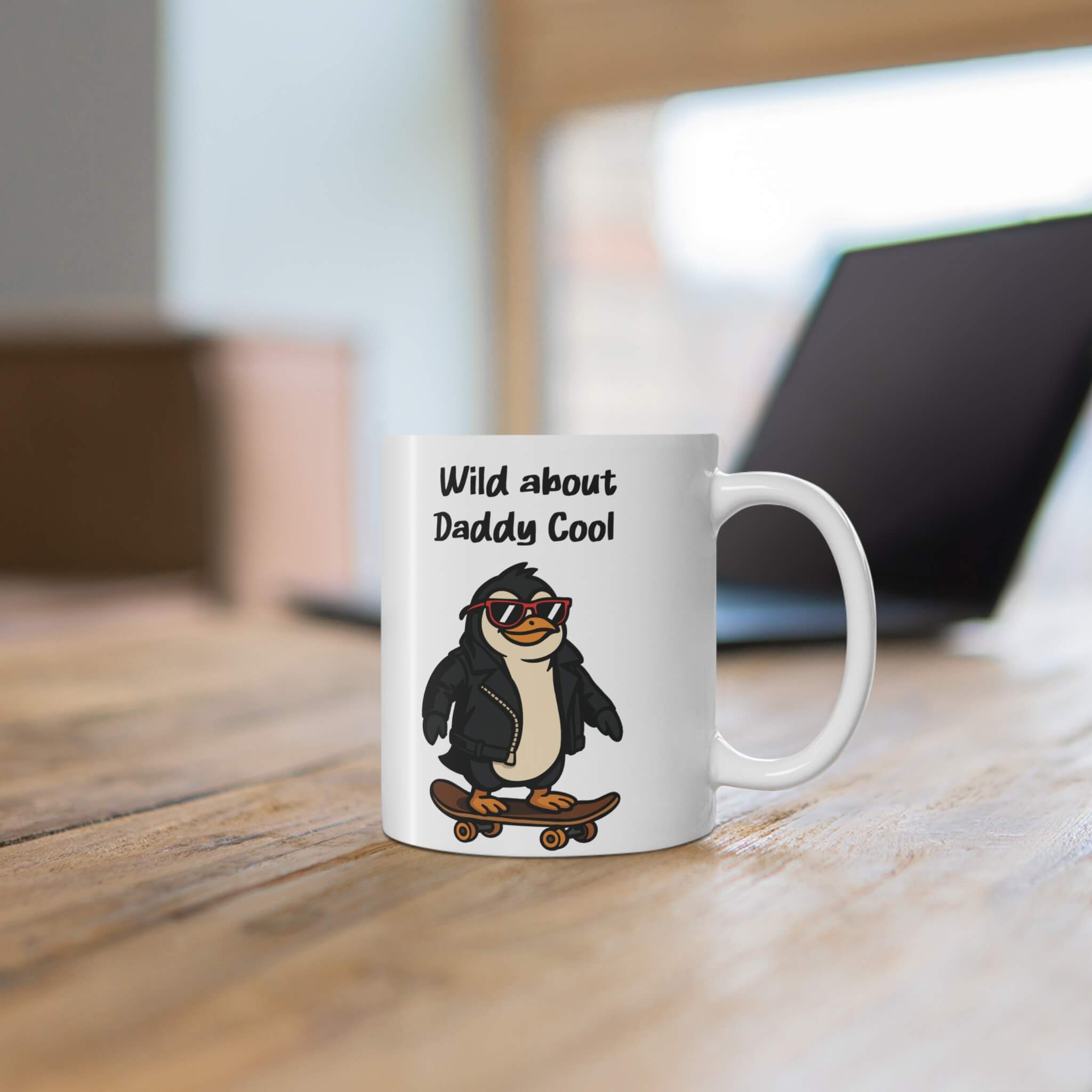 White ceramic mug featuring a cartoon penguin in a leather jacket and red sunglasses on a skateboard, with the text “Wild about Daddy Cool.”