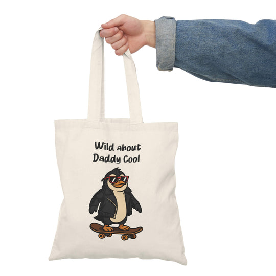 Tote bag with a cartoon penguin wearing red sunglasses and a leather jacket, riding a skateboard, with the text “Wild about Daddy Cool” above.